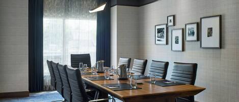 A conference room with a long table, six chairs, a coffee pot, and framed pictures on the wall.