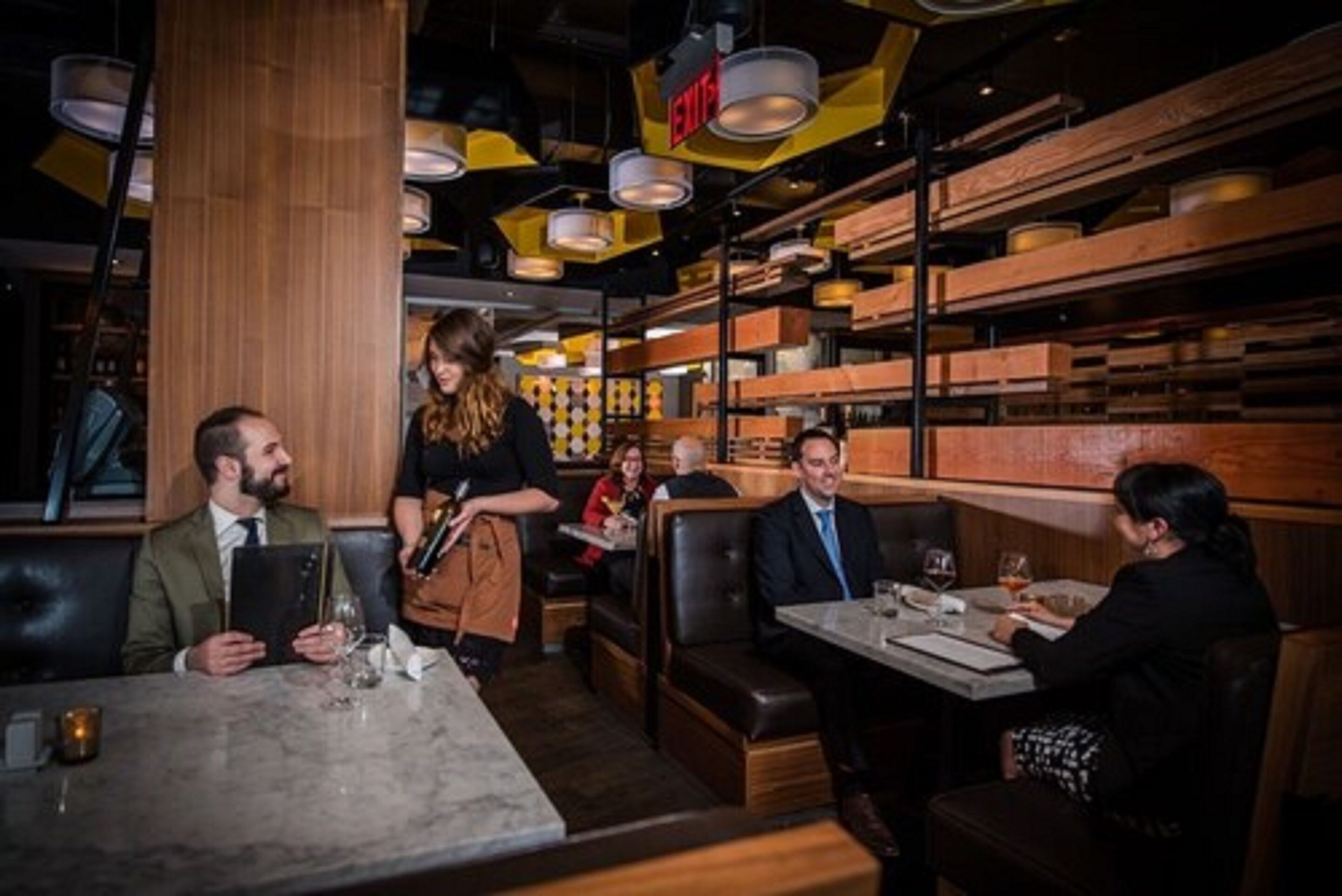Un restaurante con cabinas y mesas, estanterías de madera al fondo, y una persona sirviendo comida.