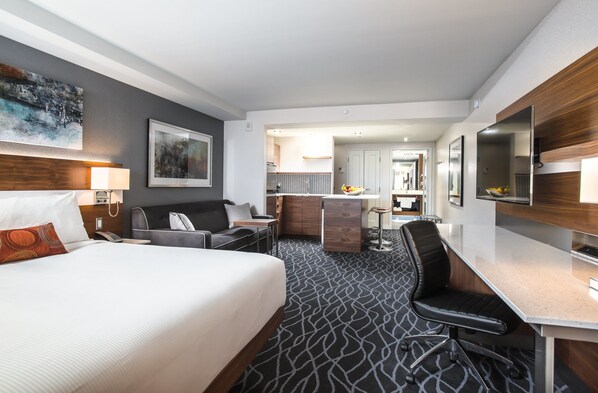A hotel room with a bed, desk, and kitchenette.