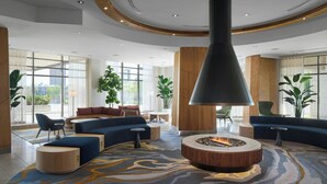 A modern lobby with a circular seating area, a central fire feature, and large windows offering views. - Delta Hotels by Marriott Waterloo (Waterloo)