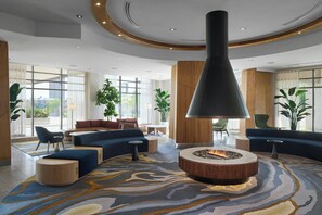 A modern lobby with a circular seating area, a central fire feature, and large windows offering views. - Delta Hotels by Marriott Waterloo (Waterloo)