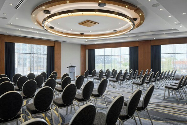 A conference room with rows of chairs, a podium, and large windows. - Delta Hotels by Marriott Waterloo (Waterloo)