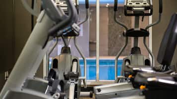 Un gimnasio con cintas de correr y elípticas, ventanas amplias con vista a una piscina e iluminación empotrada en el techo.