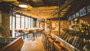 A modern restaurant interior with wooden tables and chairs, a bar area, and large windows allowing natural light. - Delta Hotels by Marriott Waterloo (Waterloo)