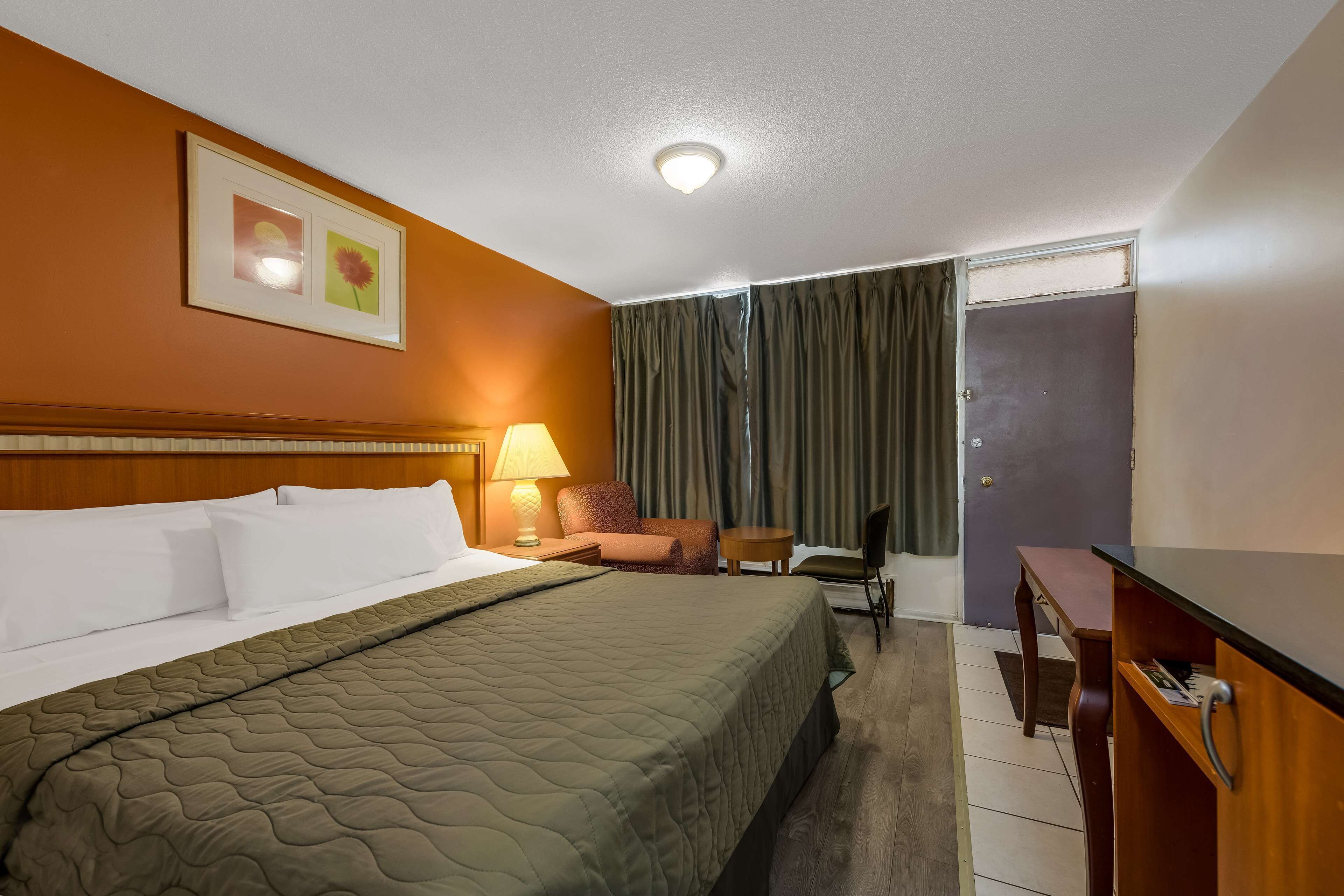 Una habitación de hotel con cama, escritorio, silla, lámpara y puerta.