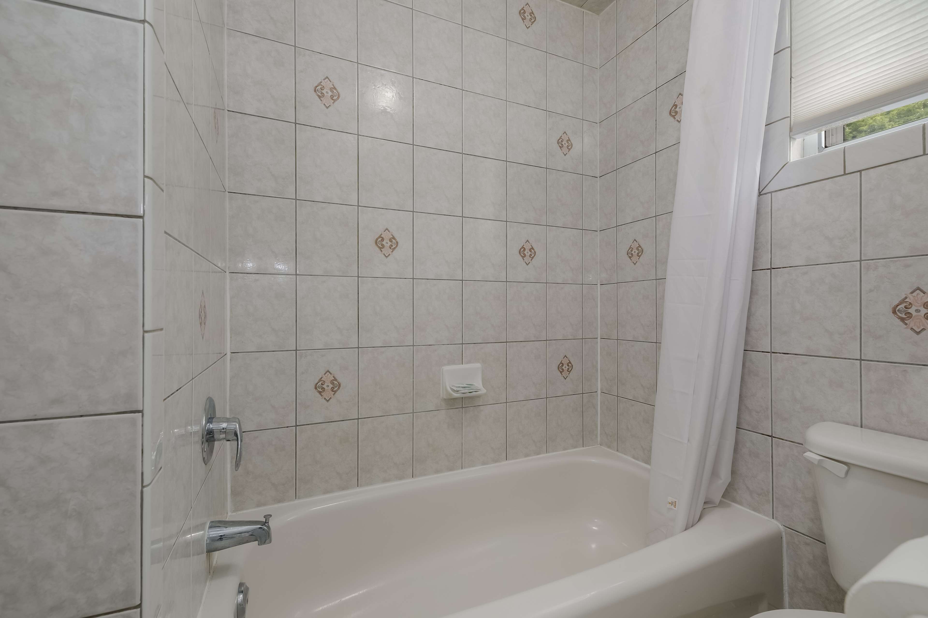 Een badkamer met een bad, witte tegels en een douchegordijn.