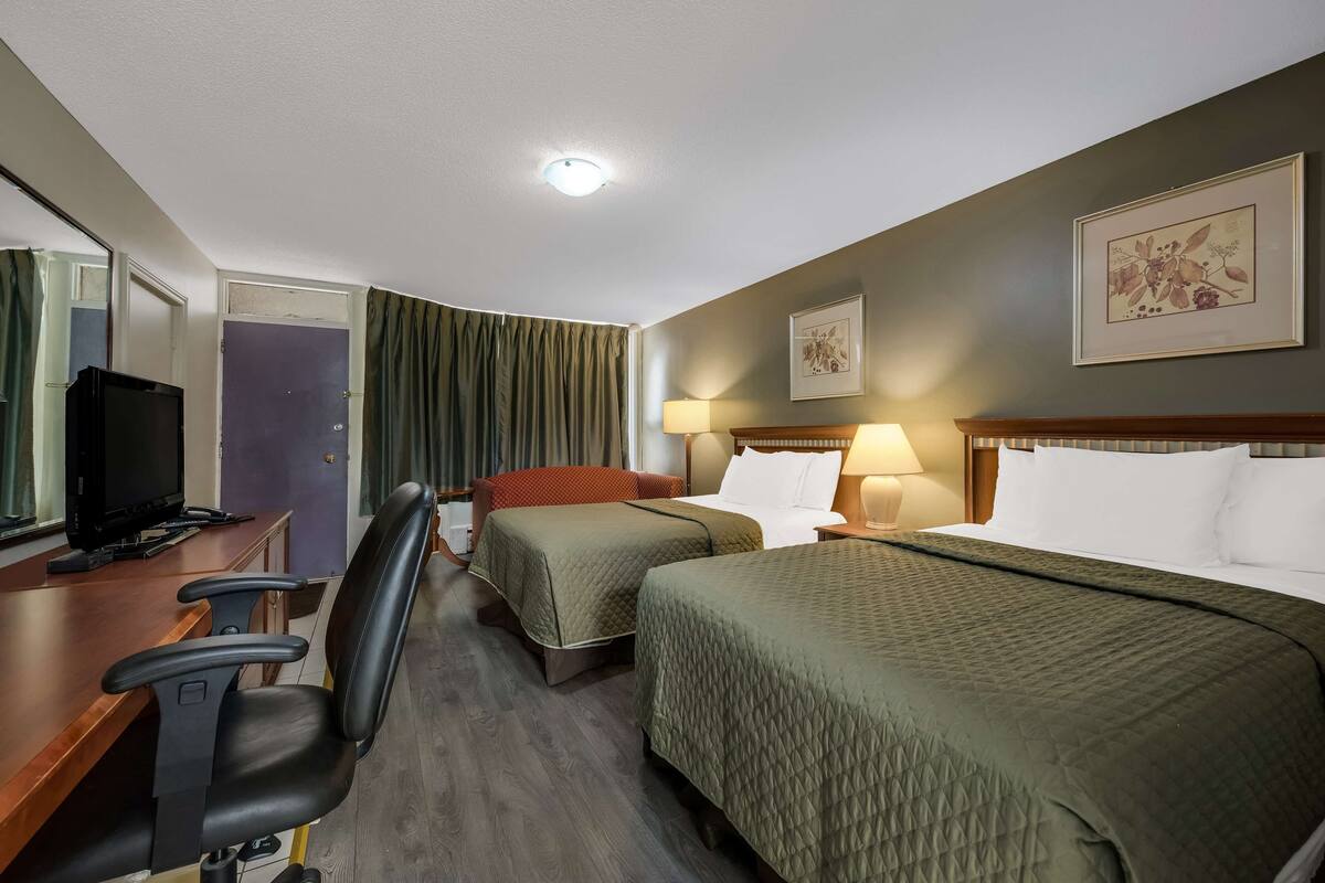 A hotel room with two beds, a desk with a computer, a chair, and a television.