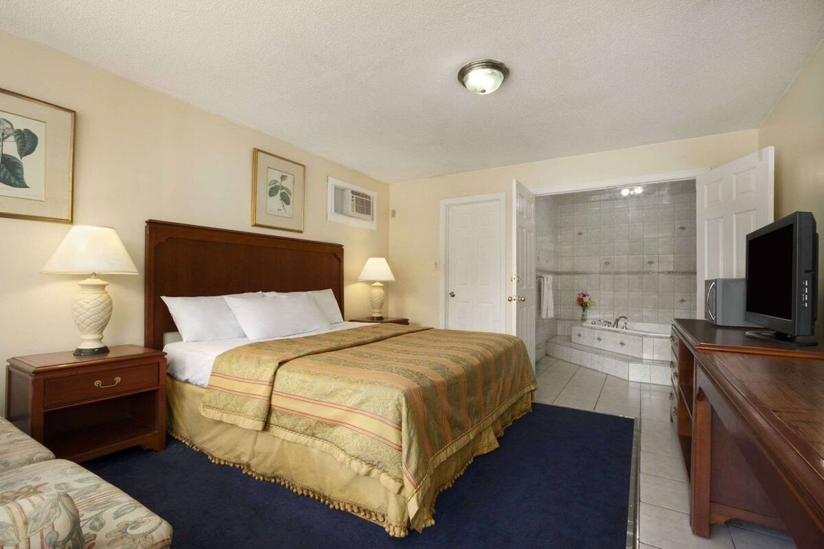 A hotel room with a bed, bedside lamps, a television, a bathroom with a bathtub, and a shower.