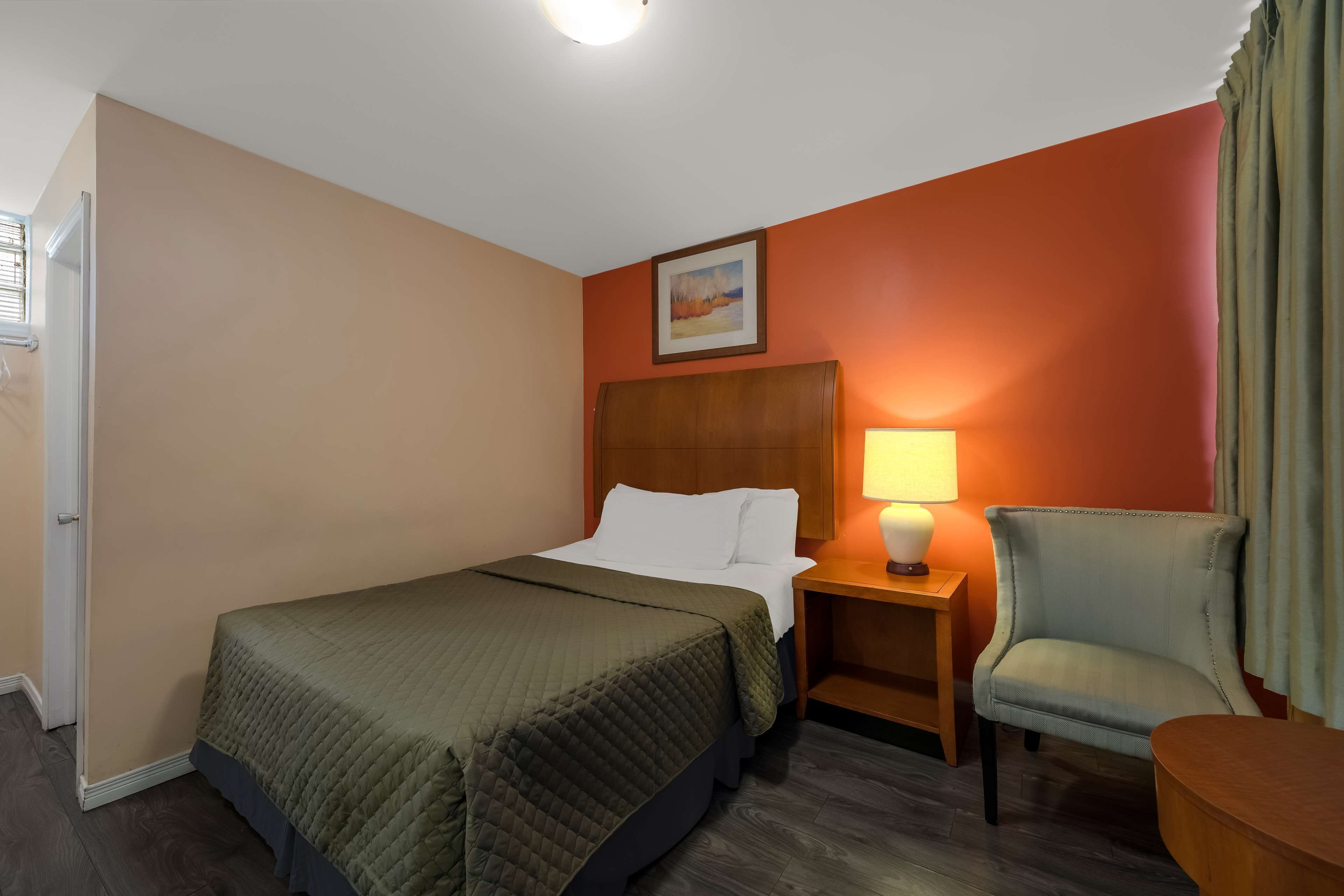 A hotel room with a bed, a nightstand, a chair, and a painting on the wall.