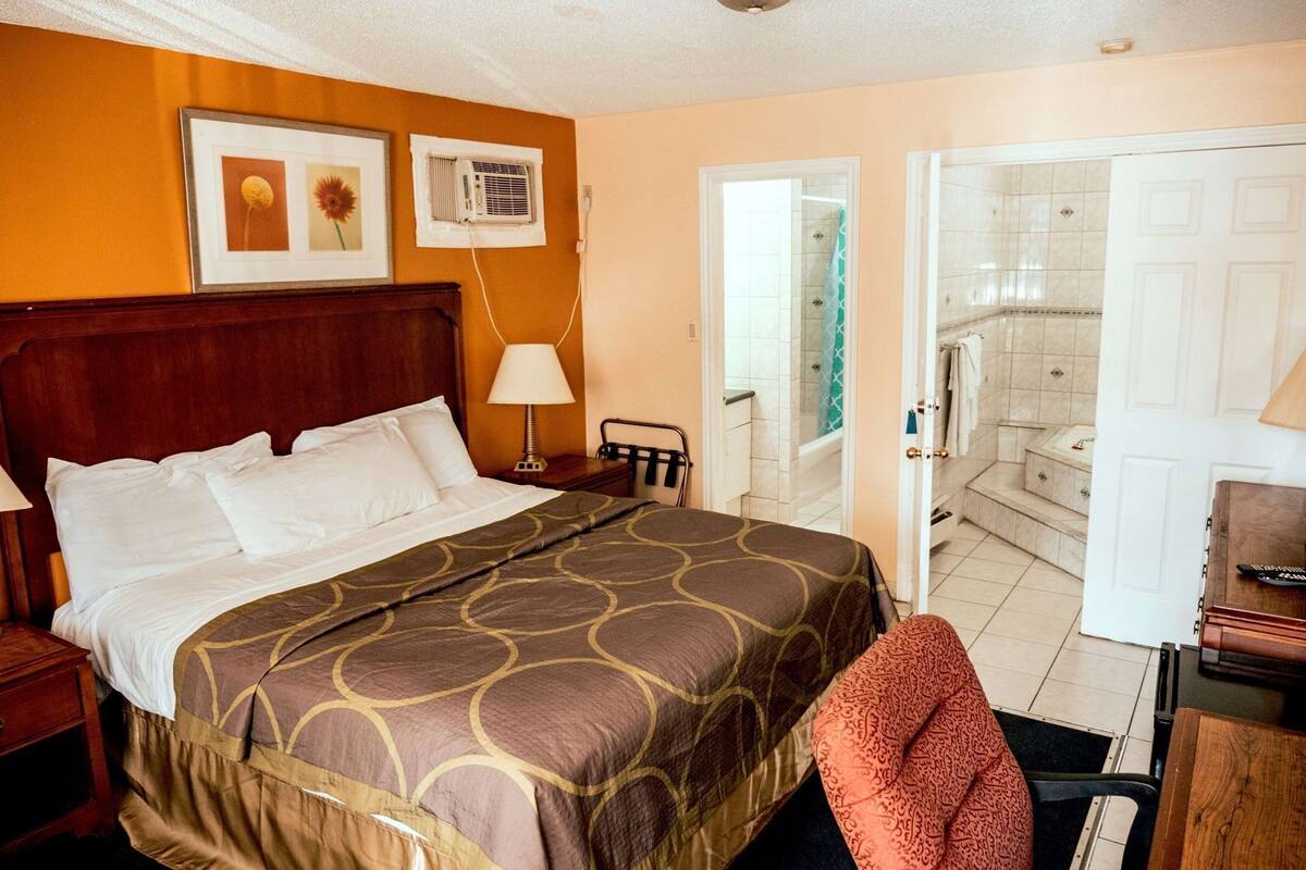 A hotel room with a bed, bedside table, lamp, and a view of the bathroom.