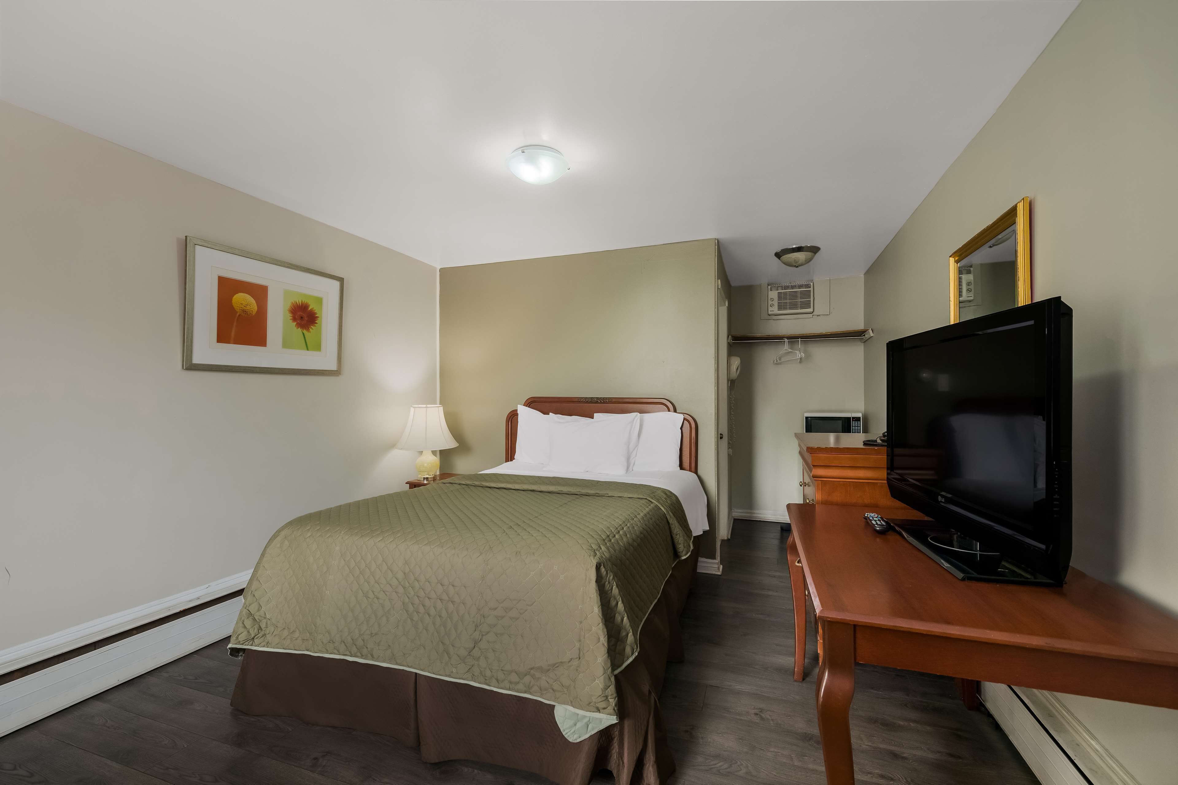 A hotel room with a bed, a TV, a desk, and a framed picture on the wall.