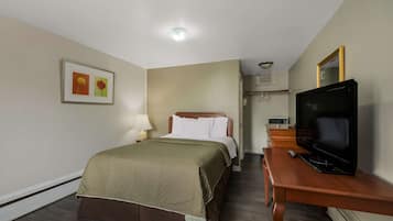 Ein Hotelzimmer mit Bett, Fernseher, Schreibtisch und einem gerahmten Bild an der Wand.