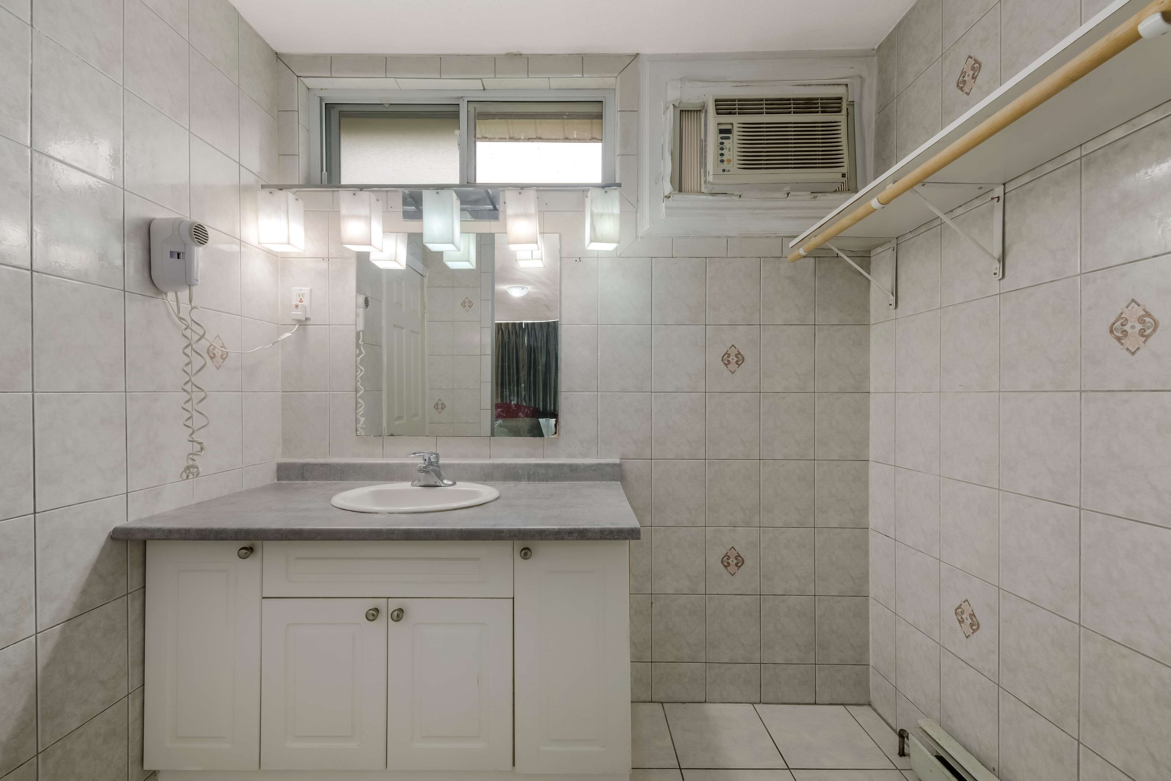 A bathroom with a white sink, mirror, and tiled walls. There is a towel rack and a shower area.