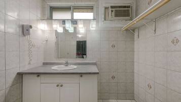 A bathroom with a white sink, mirror, and tiled walls. There is a towel rack and a shower area.