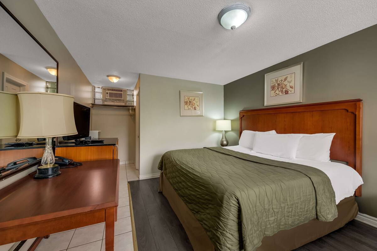 A hotel room with a bed, a desk, a lamp, and a mirror.