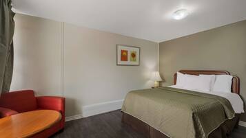 A hotel room with a bed, a nightstand, a lamp, a red sofa, and a wooden table.