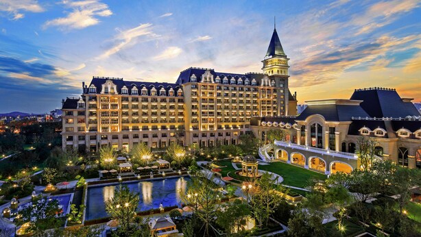 A large hotel with multiple floors, a prominent tower, and a well-maintained garden with a pool. - Hilton Qingdao Golden Beach (Qingdao)