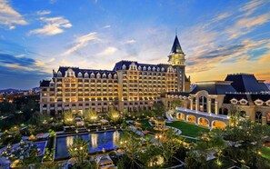 Un hotel grande con varios pisos, una torre destacada y un jardín cuidado con piscina.