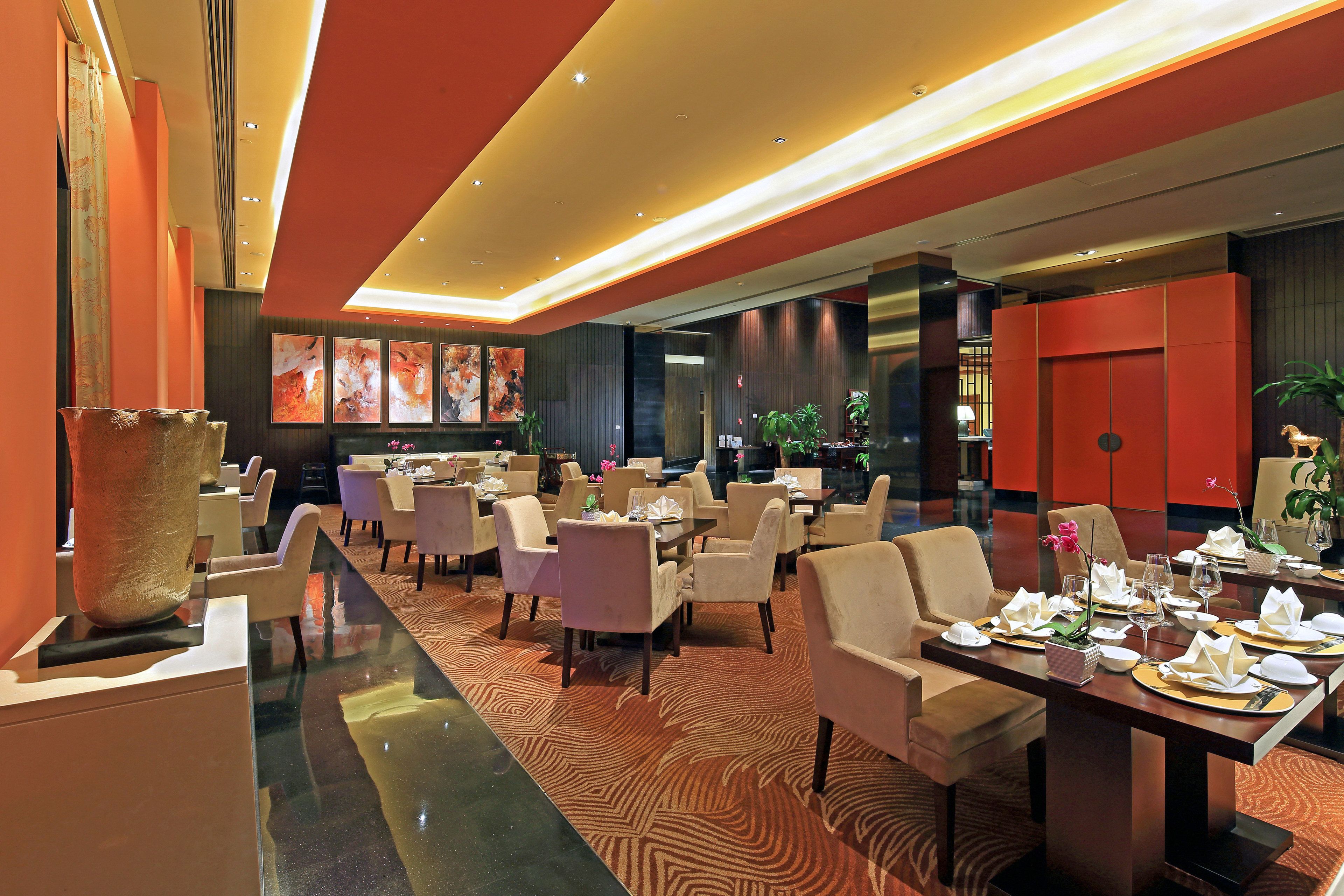 A modern restaurant with a long dining table, multiple chairs, and a large vase centerpiece.