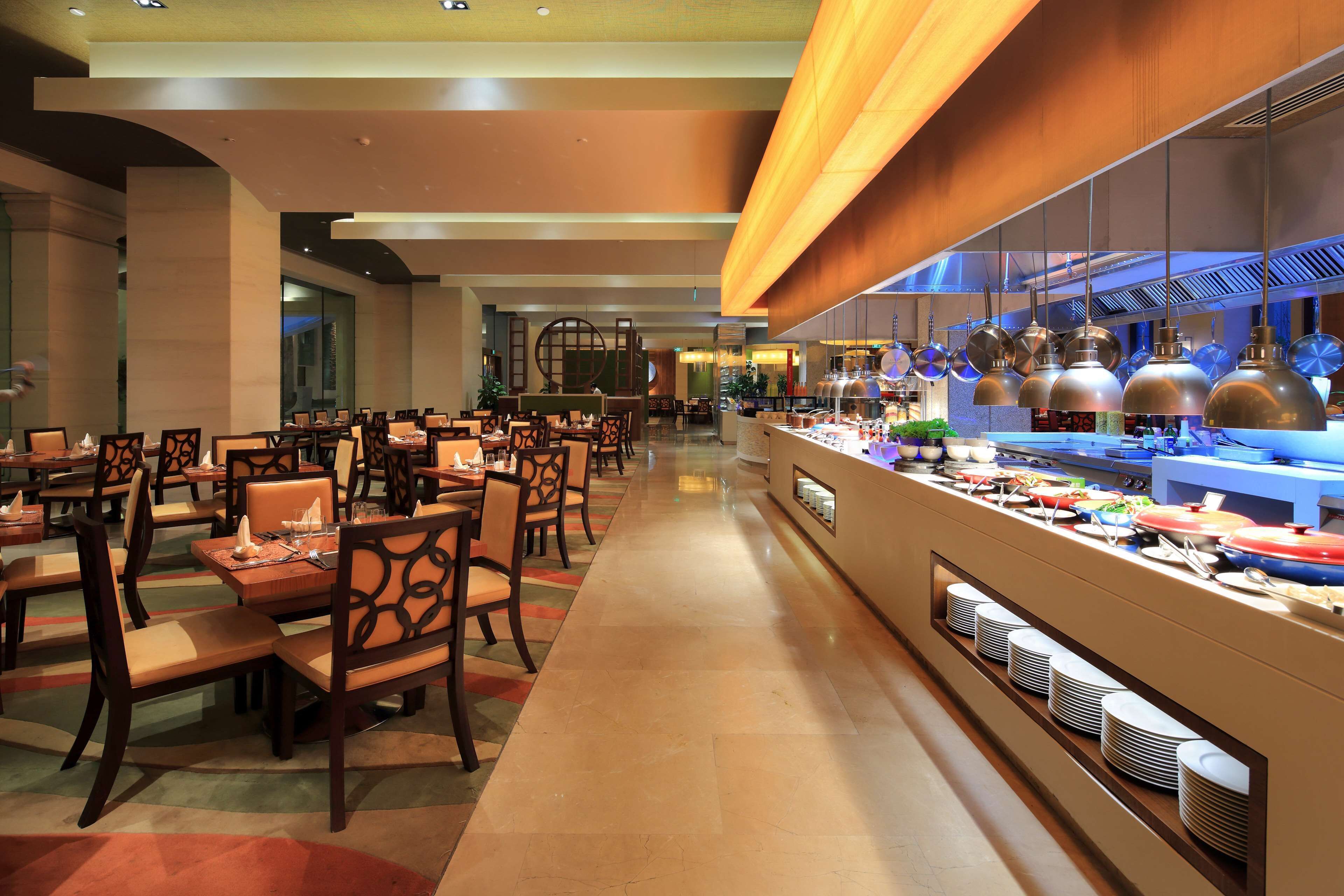 Un'ampia sala da pranzo d'hotel con numerosi tavoli e sedie, un banco buffet con diverse pietanze e un moderno design del soffitto.