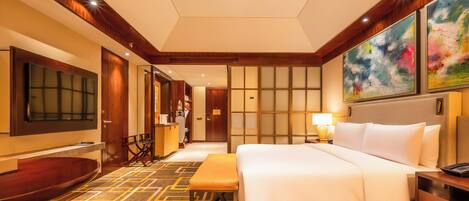 A hotel room with a large bed, a desk, a TV, and a seating area.