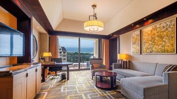 A hotel room with a large window, a sofa, a dining table, and a TV.