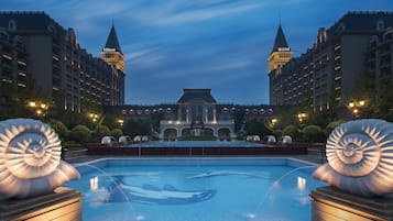 A hotel with a large swimming pool, two towers, and a fountain.