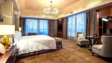 Una habitación de hotel con una cama grande, dos sillones, una mesita, una lámpara y un televisor.