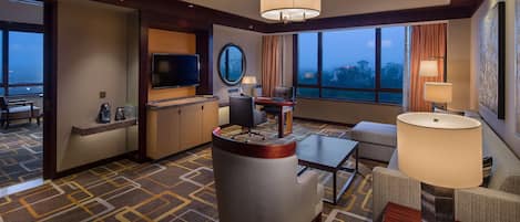 Une chambre d’hôtel dotée d’une grande fenêtre, d’un téléviseur à écran plat, d’un bureau avec une chaise, d’un canapé et d’une lampe.