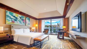 A hotel room with a large bed, a desk, a chair, a TV, and a balcony with a view.