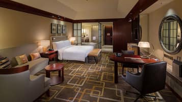 Une chambre d’hôtel avec un lit, un canapé, un bureau et une chaise. Il y a un miroir sur le mur et une porte qui donne sur une autre pièce.
