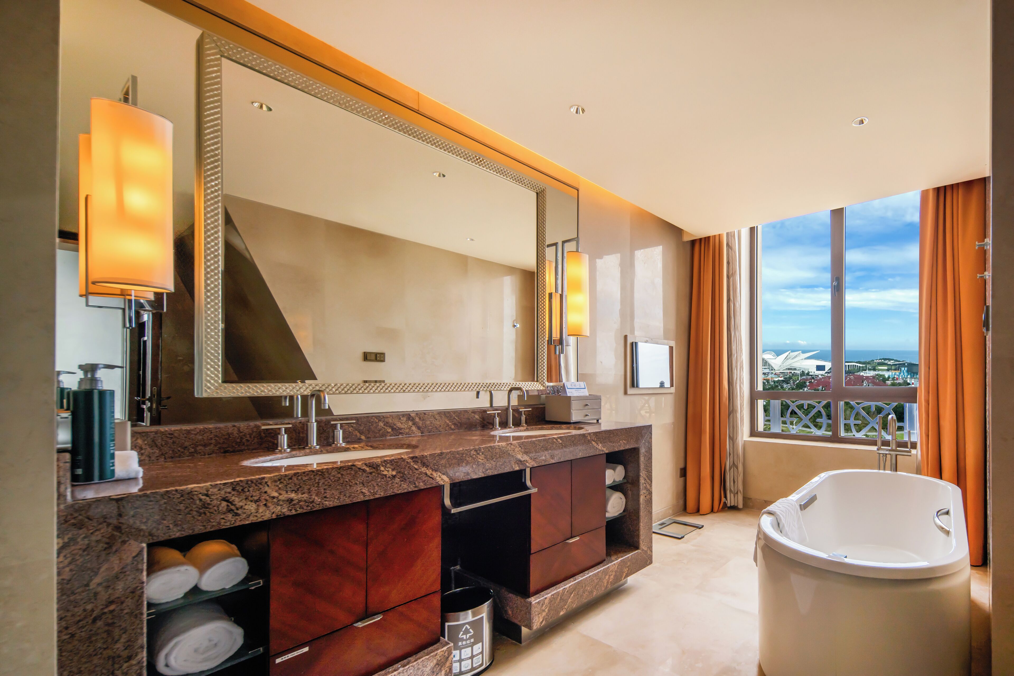 A modern bathroom with a large mirror, dual sinks, a bathtub, and a view of a landmark building.