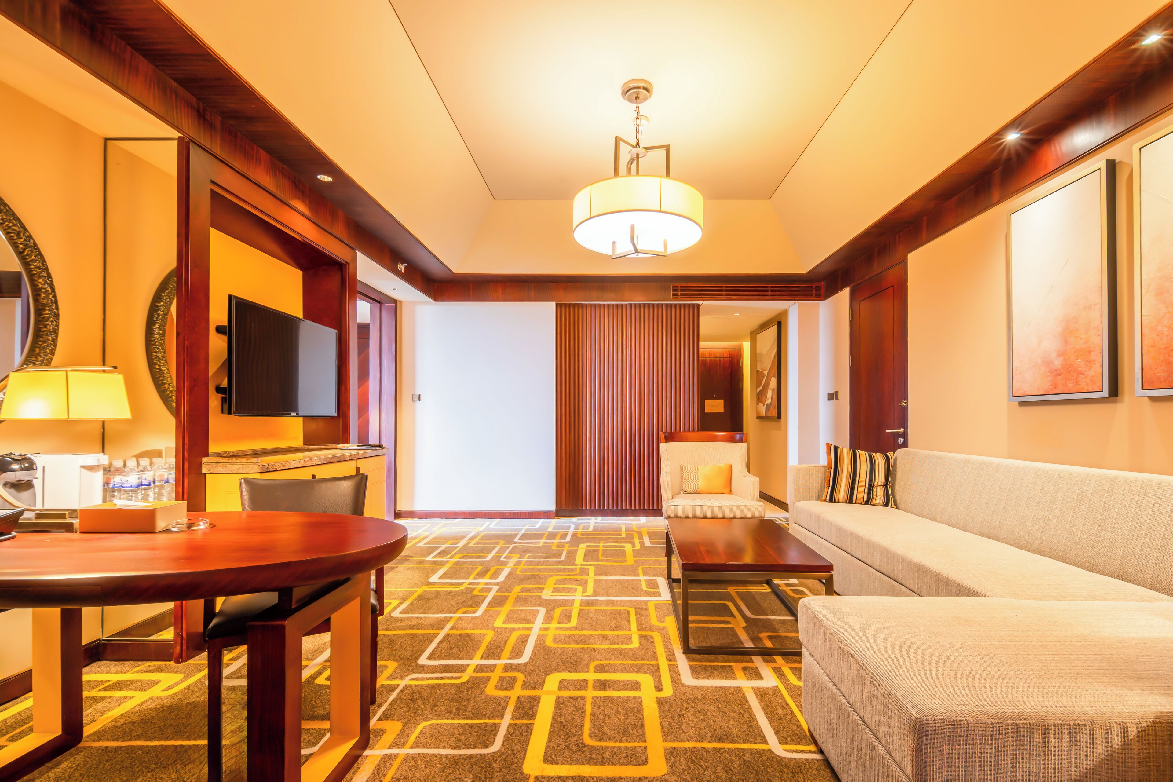 A hotel lobby with a round table, a sofa, a TV, and a patterned carpet.