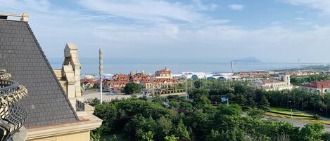 A view of a coastal city with a prominent building featuring a turret and a decorative fountain.
