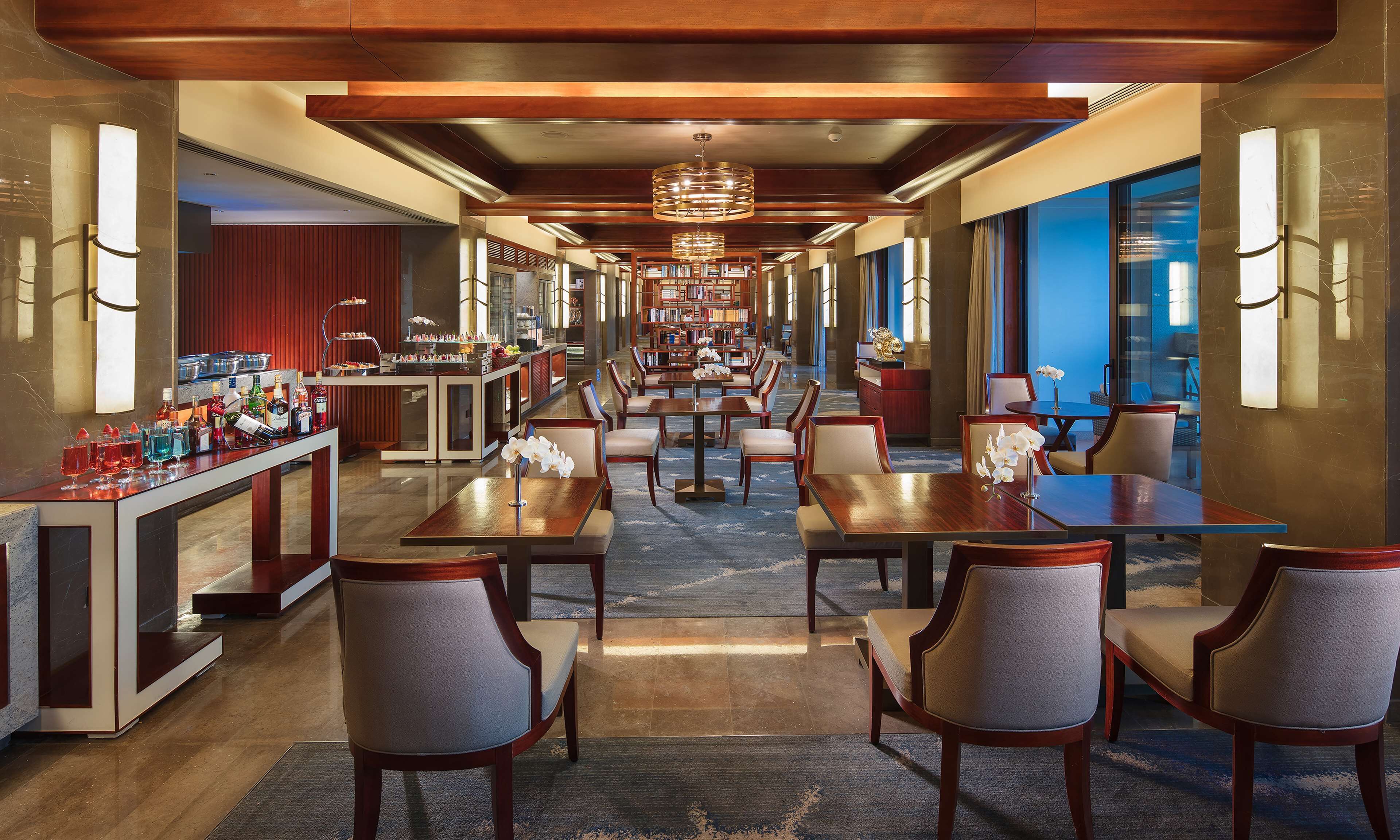 A hotel lobby with a long reception desk, multiple seating areas, and a large bookshelf.