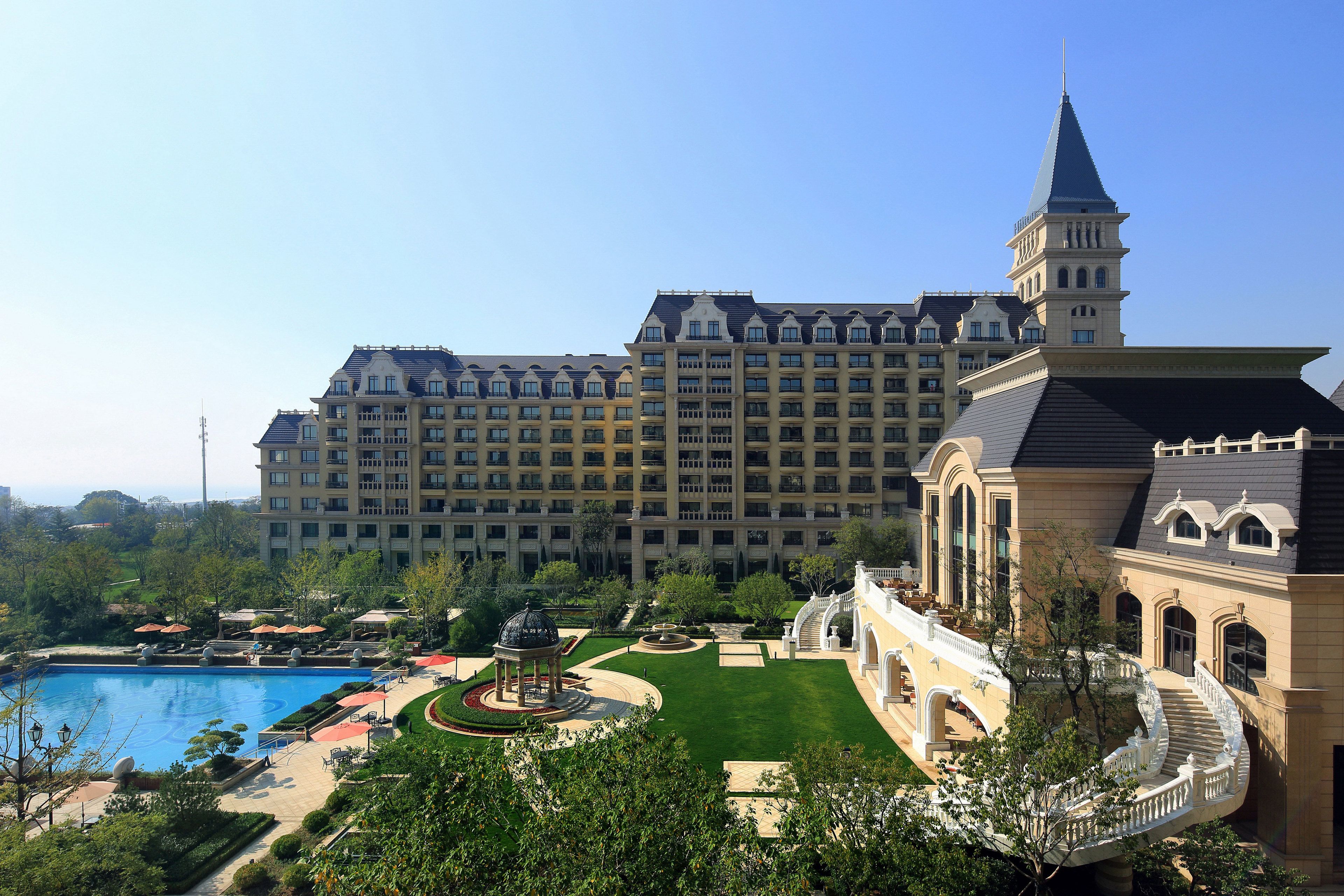 A large hotel with a swimming pool, manicured gardens, and a grand staircase.