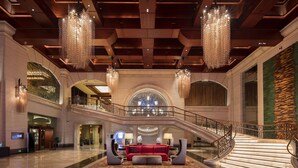 A spacious lobby with a grand staircase, chandeliers, and a red sofa. - Hilton Qingdao Golden Beach (Qingdao)
