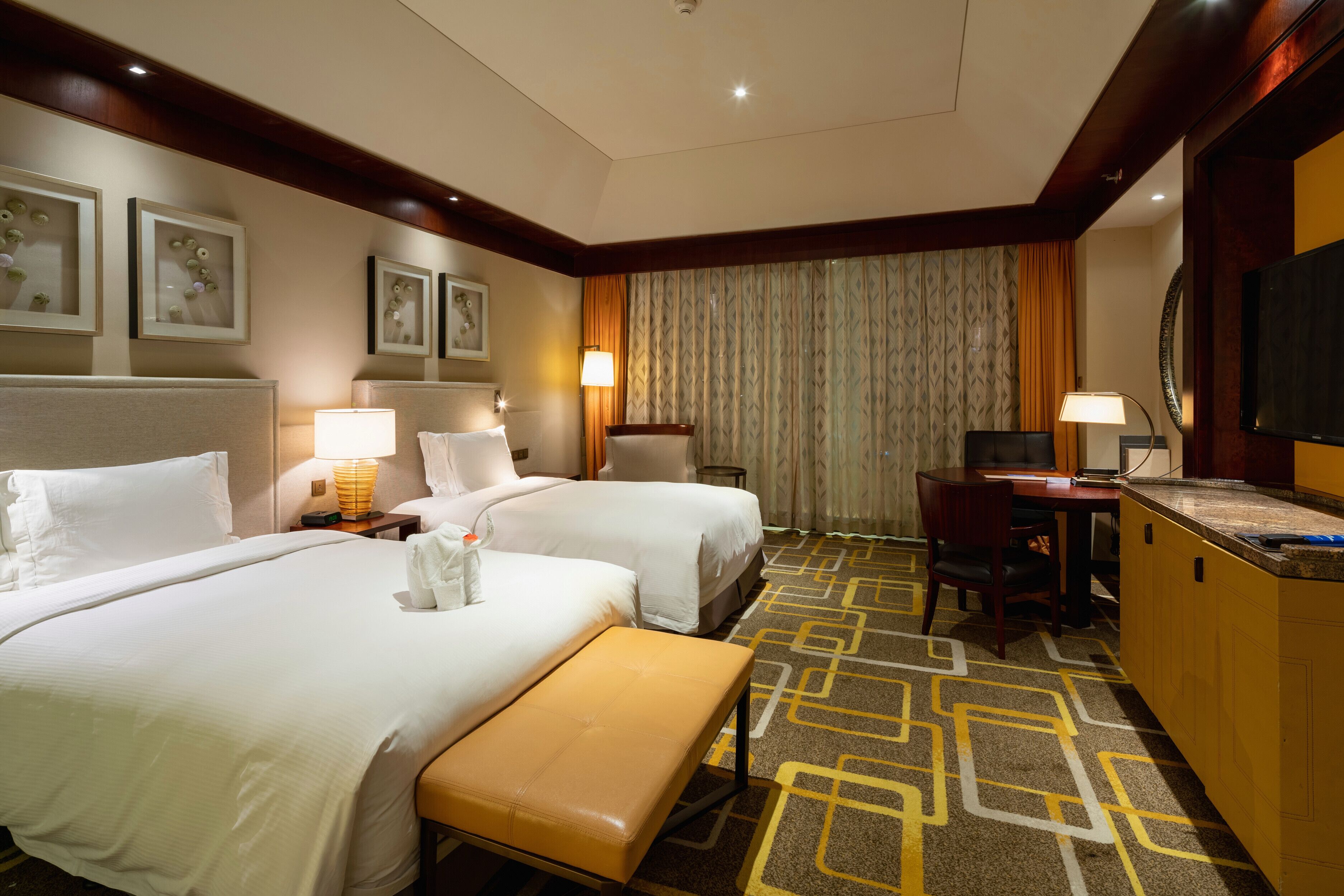A hotel room with two beds, a desk, a chair, a television, and a bathroom with a shower and toilet.