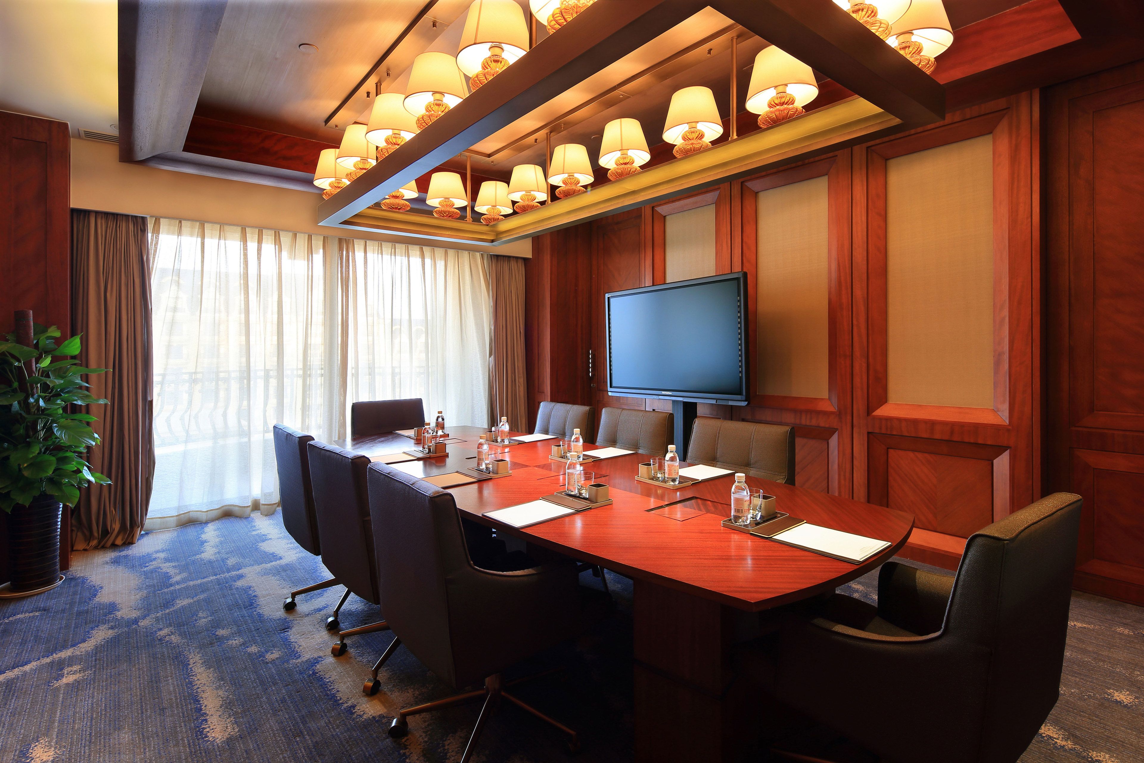 A conference room with a large table, chairs, a television, and a potted plant.