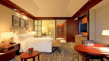 Una habitación de hotel con cama, mesita de noche, lámpara, silla y una pequeña mesa con un jarrón de flores.