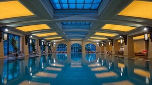 A large indoor swimming pool with a high ceiling and skylights, surrounded by seating areas and large windows. - Hilton Qingdao Golden Beach (Qingdao)