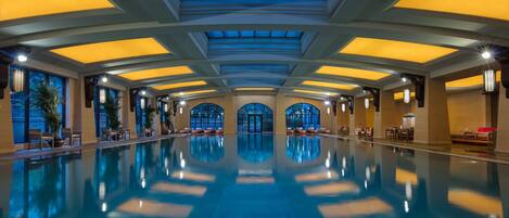 Ein großer, überdachter Pool mit hoher Decke und Oberlichtern, umgeben von Sitzbereichen und großen Fenstern.