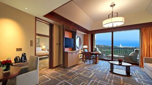 A hotel room with a bed, a desk, a chair, a sofa, a coffee table, and a view of the ocean. - Hilton Qingdao Golden Beach (Qingdao)