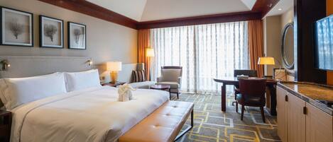 A hotel room with a large bed, a bench, a desk with a chair, a TV, and framed artwork on the wall.