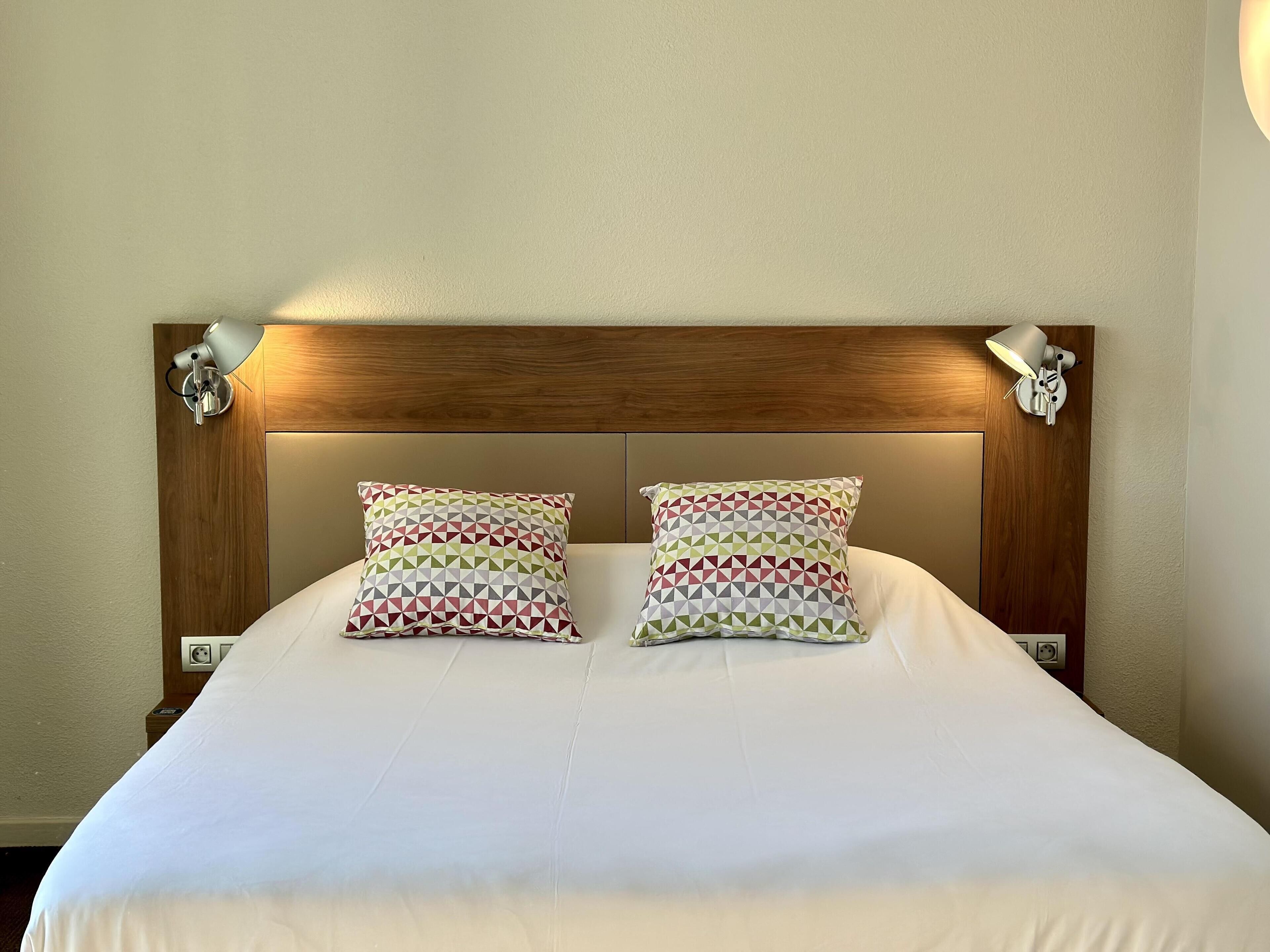 Una cama bien hecha con dos almohadones estampados y un cabecero de madera.
