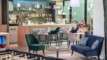 Ein moderner Barbereich mit Sitzgelegenheiten, einem Kicker und einer Bar mit verschiedenen Flaschen sowie einer Kaffeemaschine.