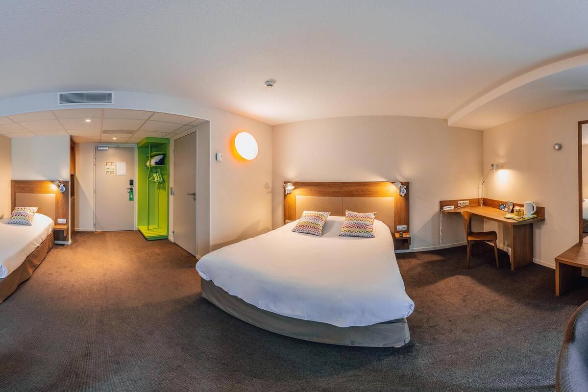 Ein Hotelzimmer mit Bett, Schreibtisch, Stühlen, Fernseher und Spiegel.