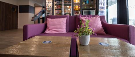 Un área de recepción con un sofá púrpura, una mesa de madera con una planta y un Mini Comptoir al fondo.