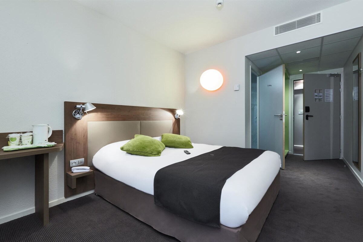 A hotel room with a bed, bedside table, lamp, and a wall-mounted light.