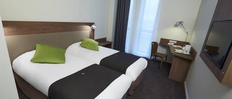 Una habitación de hotel con dos camas, un escritorio, una silla, un televisor y una ventana con cortinas.